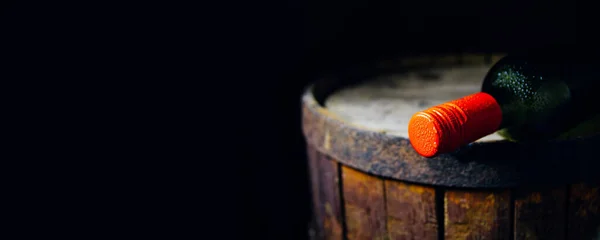 Eski bir fıçının üzerinde kırmızı bir tıpası olan bir şarap şişesi.