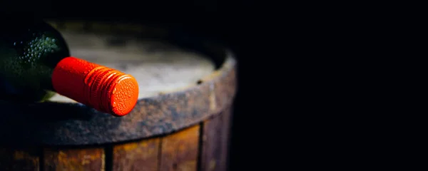 A wine bottle with a red stopper on an old wooden barrel