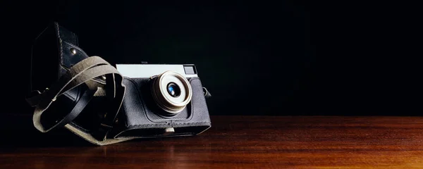 Vintage camera in a case on a wooden table on a dark background