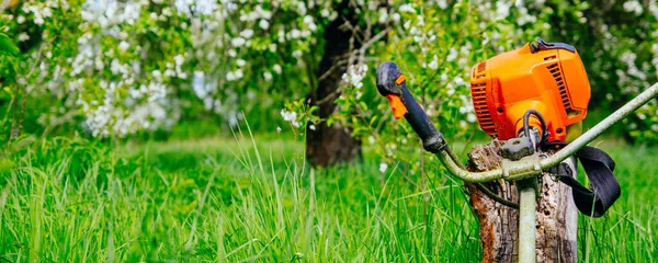 開花した庭の背景に緑の芝生の上のガソリントリマー — ストック写真