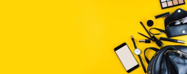 Sarı arka planda siyah kadın çantası ve aksesuarları. Düz konum ve üst görünüm, metin veya tasarım için boşluk kopyala