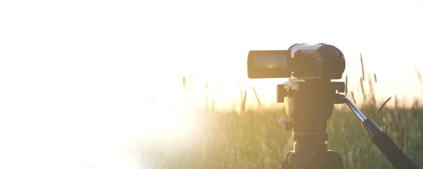 An old video camera on a tripod is set in a field with a sunset background