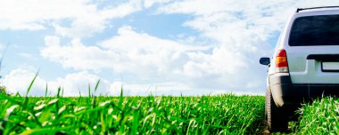 Yeşil bir tarlada, bulutlu mavi bir gökyüzüne karşı giden bir arazi aracı.