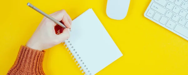 The hand of a left-handed woman holds a pencil in her hand. International concept for a left-handed person on a yellow background