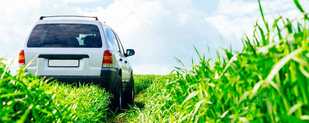 SUV car on the road in a green field against a blue sky with clouds