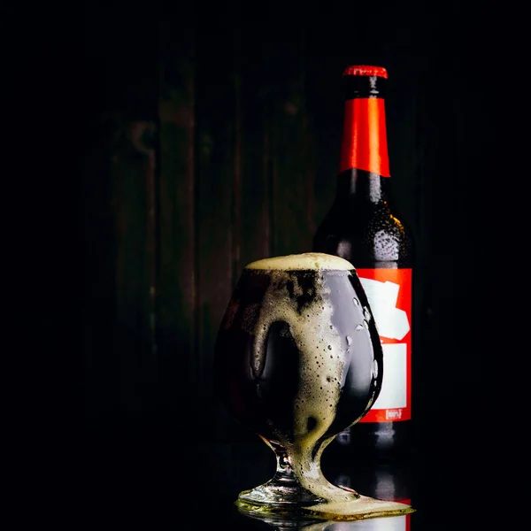 Bir bardak bira ve siyah arka planda bir şişe.