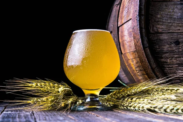 Bardakta hafif bira, buğday kulakları ve arka planda eski bir fıçı.