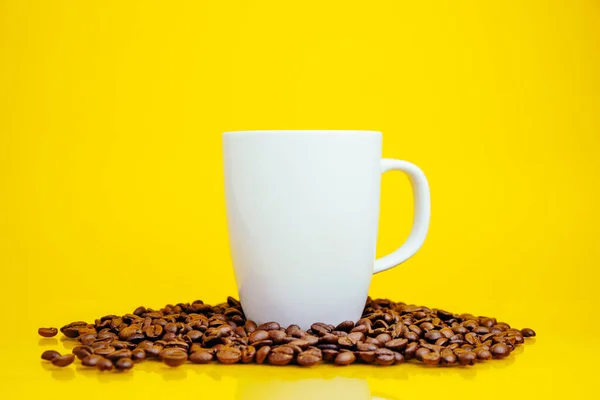 Kahve çekirdekleri ve parlak sarı arka planda beyaz bir kupa.