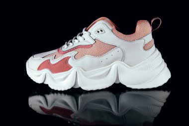 Siyah arka planda beyaz ve pembe spor ayakkabılar.