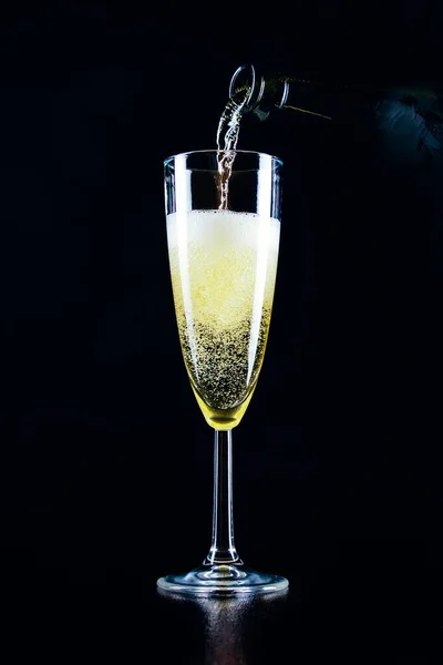 Köpüklü şarap bir şişeden koyu bir arka planda bir bardağa dökülür.