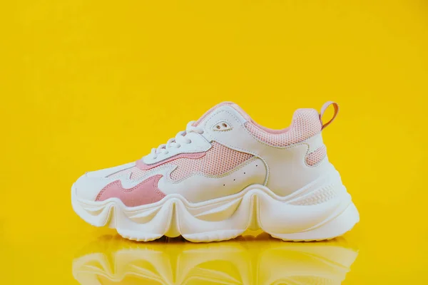 Sarı arka planda beyaz ve pembe spor ayakkabılar.