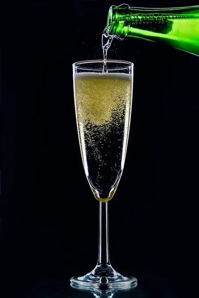 Köpüklü şarap bir şişeden koyu bir arka planda bir bardağa dökülür.