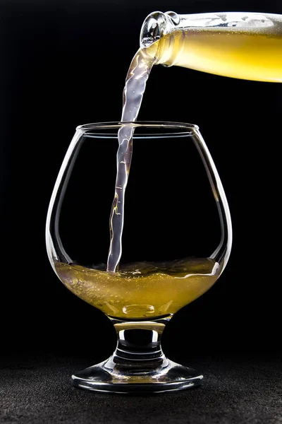 Meyve birası şişeden koyu bir arka planda bardağa dökülür.