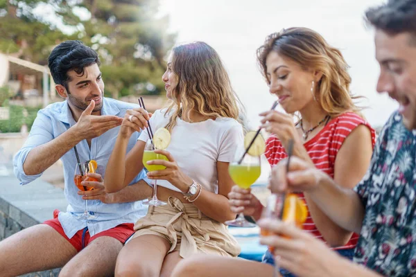 夏には屋外のベンチに座って熱帯カクテルを飲みながら話をする若者たちのトレンディーなグループ — ストック写真