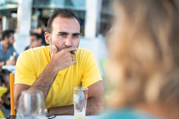 Bu arada adam konuşuyor ve en iyi arkadaşlarını bir restoranda oturmuş puro içip bira içerken dinliyor. Bir yaz barında açık havada çekim..