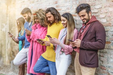 Şık arkadaşlar duvarın karşısında akıllı telefonları izlerken eğleniyorlar. İnternet ve sosyal medya uygulamalarını kullanan mutlu gençler.