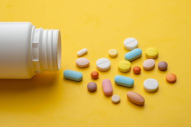 Beyaz plastik şişe ve sarı arka planda bir sürü farklı hap. 