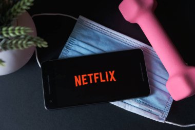 ekranda Netflix uygulaması olan cep telefonu, evde kal ve covid yüz maskesi 
