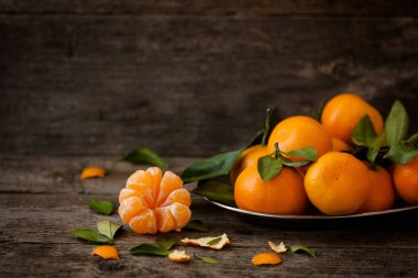 Koyu ahşap arka plan üzerinde bir tepsi üzerinde yeşil yaprakları ile taze mandalina. Temizlenmiş ve demonte içine dilim mandalina ön planda. Doğal tarzı. Yatay fotoğraf. Kopya alanı
