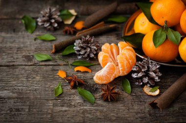 Noel ve yeni yıl atmosferini: taze mandalina yeşil yaprakları koyu ahşap arka plan üzerinde. Mandarin soyulmuş ve demonte dilimleri, tarçın, koniler, mandalina kabukları, yaprakları. Kaba ahşap dokulu arka plan. Rustik, natur
