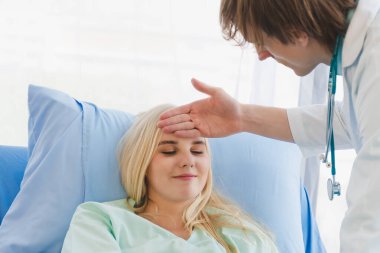 Hastane odasında kadın bir hastanın alnındaki ateşi kontrol eden bir erkek doktor. Tıp kavramı, hastanede sağlık..