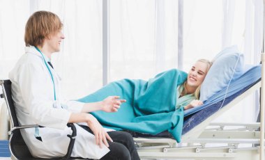 Genç bir doktor, yatakta neşe ve dostlukla yatan bir kadın hastayla konuşuyor. Hastanedeki sağlık hizmetlerinin resmi.