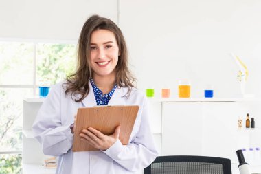 Bir kadın bilim adamı, bilim laboratuarında sonuçlarının bir kaydını tuttuğu için gülümsüyor ve panoyu tutuyor..