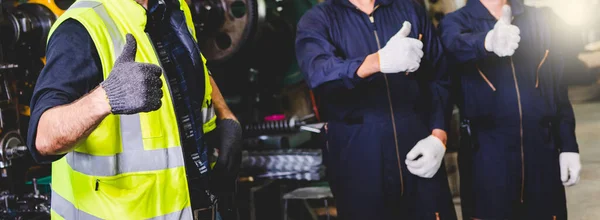 Fabrika mühendisi ayakta duruyor ve fabrikanın içinde çalışırken başparmağını gösteriyor. Fabrikada çalışan endüstriyel işçiler..