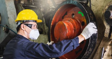 Üniformalı, kasklı, eldivenli ve maskeli Asyalı fabrika mühendisi torna tezgahıyla fabrikada sıkı çalışıyor..