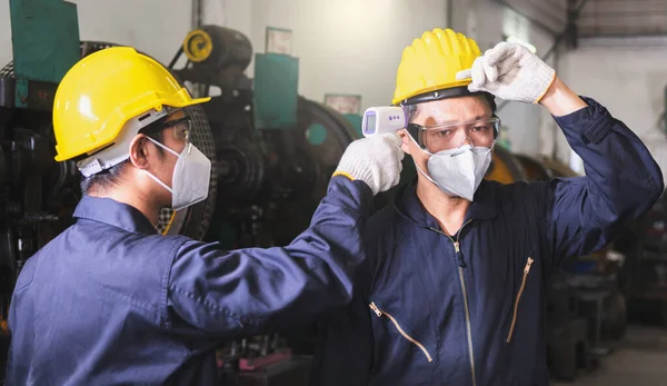 Endüstriyel tesise girmeden önce yüz maskesi, eldiven ve tarama işçisi takan erkek işçi COVID 19 'u fabrikadaki işçiye korumak için endüstriyel tesise giriyor..