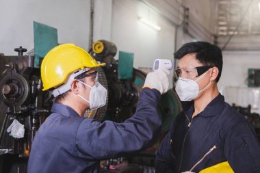 Endüstriyel tesise girmeden önce yüz maskesi, eldiven ve tarama işçisi takan erkek işçi COVID 19 'u fabrikadaki işçiye korumak için endüstriyel tesise giriyor..