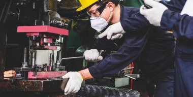 Metal fabrikası mühendisleri, kasketli, maskeli ve eldivenli. Tablet bilgisayarlarını endüstriyel bir tesisin içinde tornalı metal parçaları üretmek için tutuyorlar..