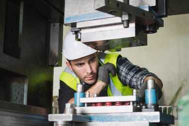 Kafkas erkek bir makine mühendisi fabrikadaki metal işleri için makineyi kontrol ediyor. Bir mühendis kask takıyor ve metal endüstrisinde makine üzerinde çalışıyor..