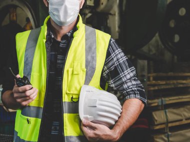Fabrika mühendisi üniformalı bir başlık ve haberleşme telsizini endüstriyel alanda çalışmaya hazır hale getirmek için tutuyor. Fabrikada üniformalı, kasklı, eldivenli ve anahtarlı bir sanayi işçisi..