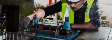 Bir fabrika erkek makine mühendisi fabrikadaki metal işleri için makineyi kontrol ediyor. Bir mühendis kask takıyor ve metal endüstrisinde makine üzerinde çalışıyor..