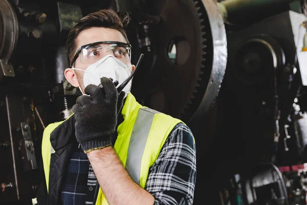 The factory engineer man that wearing a uniform and holding a communication radio to talk about controlling the mechanical machine. A smart factory worker in a uniform and holds a communication radio.