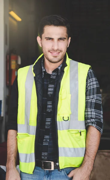 A portrait of a factory engineer in a uniform standing inside the factory. A caucasian worker is smiling while standing in the resting time of the factory life.