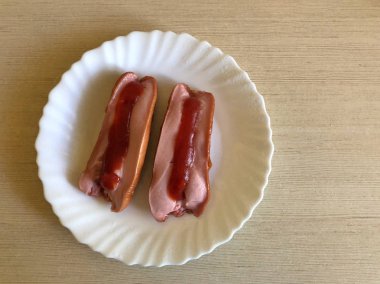 Beyaz plaka içinde ketçap ile iki kızarmış sosis