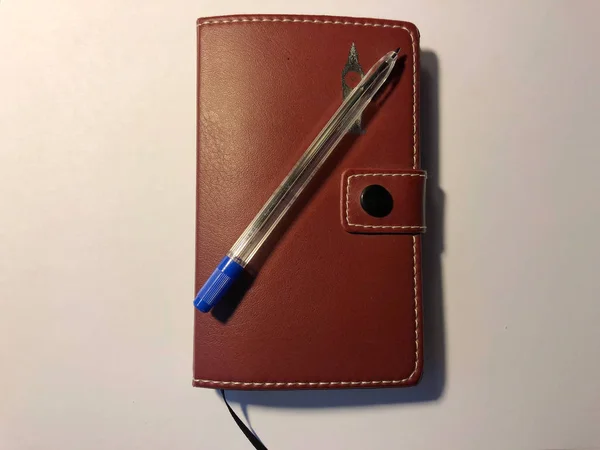 Pluma azul con un cuaderno marrón sobre un fondo blanco —  Fotos de Stock