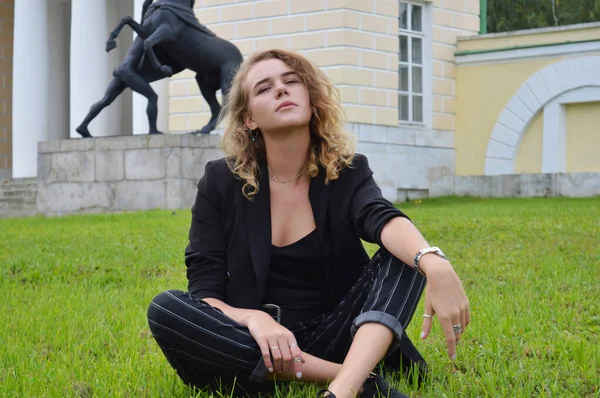 Uma jovem mulher sexy em um terno preto de negócios está sentada — Fotografia de Stock