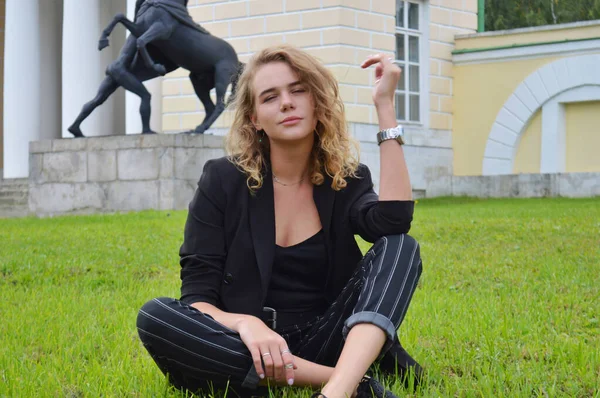 Uma jovem mulher sexy em um terno preto de negócios está sentada — Fotografia de Stock