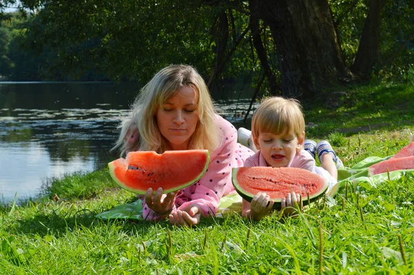 Menino com mãe na margem do rio comer melancia . — Fotografia de Stock