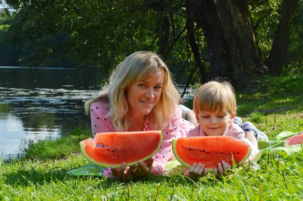 Little boy with mother on the river bank eat watermelon. — Stock Photo, Image