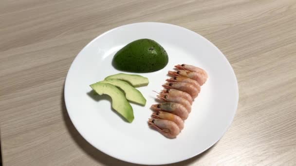 Beyaz bir tabakta karides ve dilimlenmiş avokado. Bir tabaktan avokado ve karides al. — Stok video