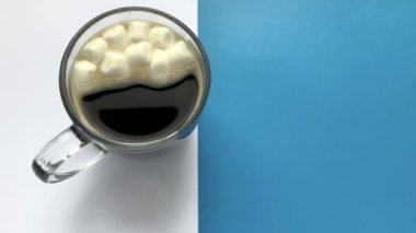 Kadın bir fincan kahveye beyaz mini marşmelov döküyor..