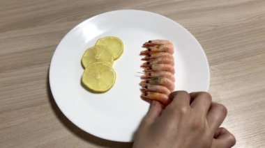 Beyaz bir tabakta karides ve dilimlenmiş limon. Karidesi temizler.
