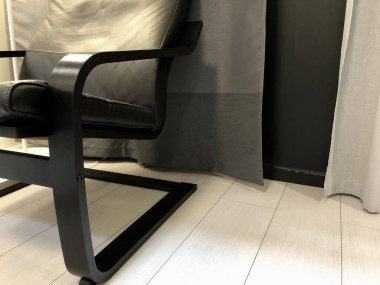 Açık ahşap bir zeminde siyah deri koltuk perde arka planda..