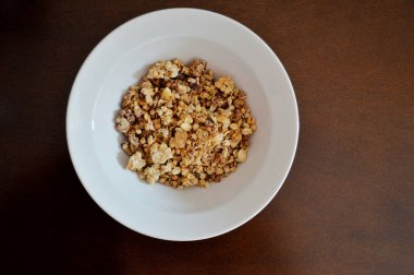 Kahverengi ahşap bir masada beyaz bir tabakta kuru müsli..