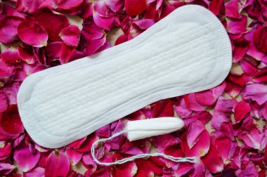 Beyaz kadın pedi ve tampon pembe gül yaprakları dokusunda yatıyor..