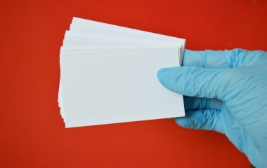 Mavi lastik eldivenli kadın eli kırmızı arka planda beyaz kartvizit tutuyor..